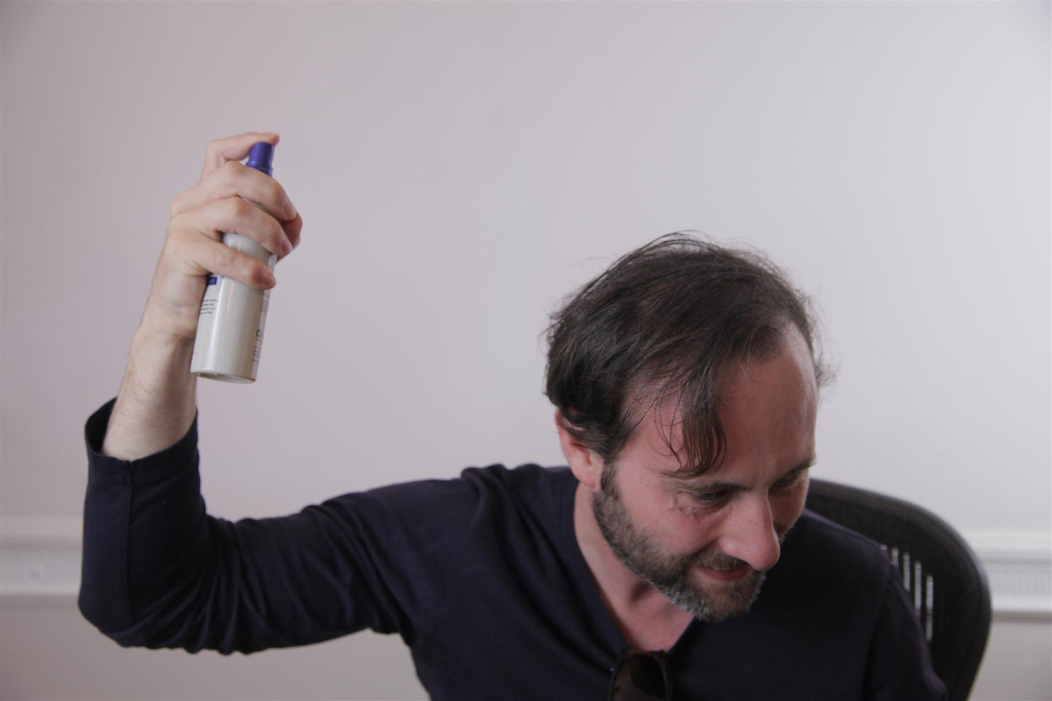 A man using KeraFiber Fiber Hold Spray to set the hair building fibers on his scalp.