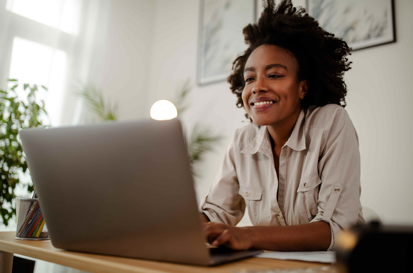 A smiling black woman with good self esteem at her workplace, looking at a laptop.